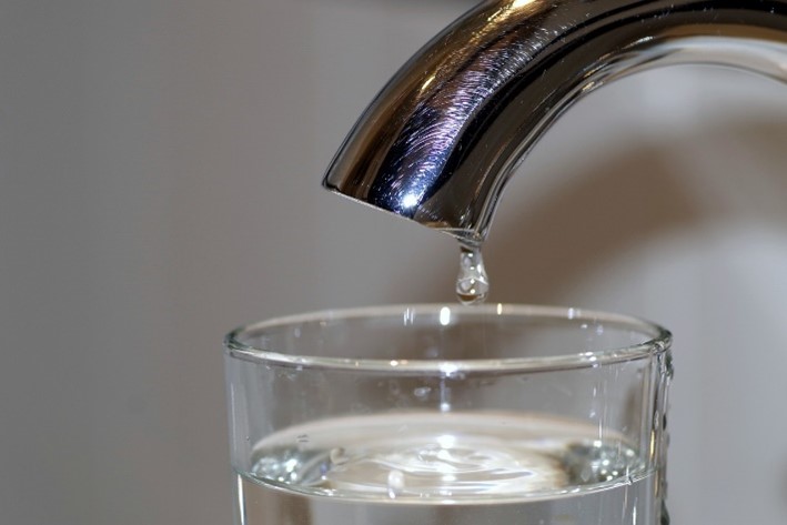 Image of a kitchen sink faucet with water dripping into a clear drinking glass.